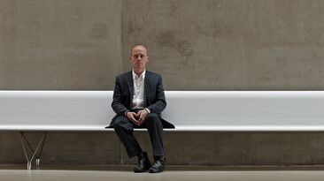 Erik graz05 Erik Spiekermann sitzt auf einer langen, weissen Bank in Graz.